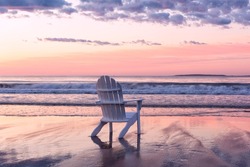 White wooden chair on the edge of the ocean at dawn. Gentle pink dawn. USA. Maine.