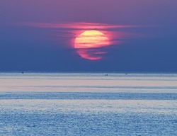sunrise over the sea. A huge bright red sun emerges from the sea. in the distance small boat on the horizon. Reflected red light on the water.
