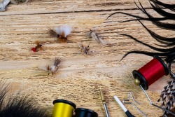 Several fly tying flies on a wooden background among fly tying materials. Fantasy dry flies for fishing.