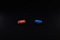 A red pill and a blue pill on black background. The concept of choice.