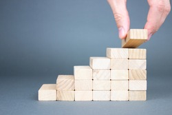 Male hand putting wooden blocks in the form of a ladder. The concept of building a success of the foundation.