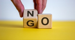 Hand flips a cube and changes the word 'no' to 'go'. Beautiful yellow table, white background. Concept. Copy space.