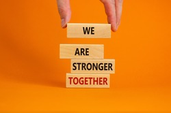 Male hand placing a block with word 'we' on a blocks tower with words 'we are stronger together'. Beautiful orange background. Business concept. Copy space.