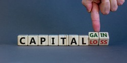 Capital loss or gain symbol. Male hand turns cubes and changes words 'capital loss' to 'capital gain'. Beautiful grey background. Business and capital loss or gain concept. Copy space.