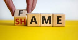Fame or shame symbol. Male hand flips wooden cubes and changes the word 'shame' to 'fame' or vice versa. Beautiful yellow table, white background, copy space. Business and fame or shame concept.