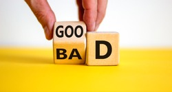 Good or bad symbol. Businessman hand turns a cube and changes the word 'bad' to 'good'. Beautiful yellow table, white background, copy space. Business and bad or good concept.