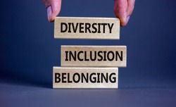 Diversity, inclusion and belonging symbol. Wooden blocks with words 'diversity, inclusion, belonging' on beautiful grey background. Male hand. Diversity, business, inclusion and belonging concept.