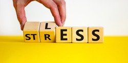 Having less stress or being stress-less. The word 'STRESS' and 'LESS' on wooden cubes. Male hand. Beautiful yellow table, white background, copy space. Business and psychological less stress concept.