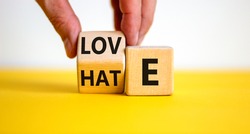 From hate to love symbol. Hand turns the cube and changes the word 'hate' to 'love'. Beautiful yellow table, white background, copy space. Valentines day and hate or love concept.