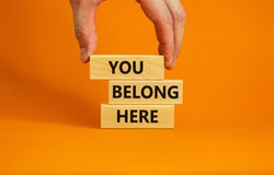 You belong here symbol. Wooden blocks with words 'You belong here' on beautiful orange background. Male hand. Diversity, business, inclusion and belonging concept.