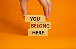 You belong here symbol. Wooden blocks with words 'You belong here' on beautiful orange background. Male hand. Diversity, business, inclusion and belonging concept.