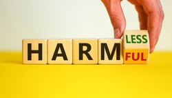 From harmful to harmless. Male hand turns the cube and changes word 'harmful' to 'harmless'. Beautiful yellow table, white background. Business and harmful or harmless concept. Copy space.