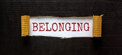 Belonging and inclusion symbol. The word 'belonging' appearing behind torn black paper. Beautiful black background. Business, inclusion and belonging concept. Copy space.