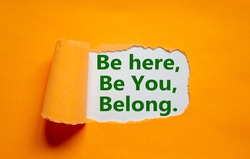 You belong here symbol. Words 'be here, be you, belong' appearing behind torn orange paper. Orange background. Business, diversity, inclusion, belonging and you belong here concept, copy space.