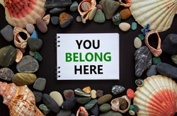 Inclusion and belonging symbol. Words you belong here on a beautiful white note, black background. Sea stones and seashells. Business, inclusion, belonging and you belong here concept.