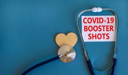 Covid-19 booster shots vaccine symbol. White card with words Covid-19 booster shots, beautiful blue background, wooden heart and stethoscope. Covid-19 booster shots vaccine concept.
