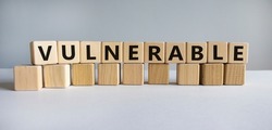 Vulnerable symbol. The word Vulnerable on wooden cubes. Beautiful white table, white background. Business and vulnerable concept. Copy space.