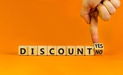 Discount symbol. Businessman turns a wooden cube and change words 'discount no' to 'discount yes'. Beautiful orange background. Business and discount concept, copy space.