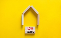 Low house rates symbol. Concept words 'Low rates' on wooden blocks near miniature house. Beautiful yellow background, copy space. Business and low house rates concept.