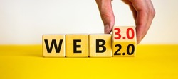 WEB 2 or 3 symbol. Businessman turns a wooden cube and changes words WEB 2.0 to WEB 3.0. Beautiful yellow table, white background, copy space. Business, technology and WEB 2.0 or 3.0 concept.