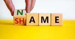 Name or shame symbol. Businessman turns the wooden cube and changes the word 'shame' to 'name' or vice versa. Beautiful yellow table, white background, copy space. Business, name or shame concept.