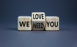We need and love you symbol. Businessman turns the wooden cube and changes words we need you to we love you. Beautiful grey background, copy space. Business, support we need and love you concept.