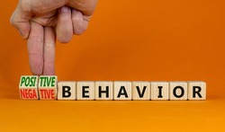 Positive or negative behavior symbol. Businessman turns cubes, changes words negative behavior to positive behavior. Orange background, copy space. Psychology, positive or negative behavior concept.