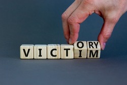 From victim to victory symbol. Businessman turns wooden cubes and changes concept words Victim to Victory. Beautiful grey background. Business support from victim to victory concept. Copy space.
