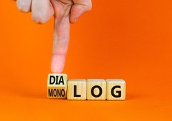 Businessman turns wooden cubes and changes the German word monolog - monologue in English to dialog - dialogue in English. Beautiful orange background. Business monolog or dialog concept. Copy space.