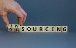 Outsourcing or insourcing symbol. Businessman turns wooden cubes and changes the word Outsourcing to Insourcing. Beautiful grey background. Business and outsourcing or insourcing concept. Copy space.