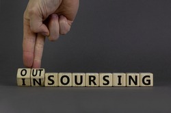 Outsourcing or insourcing symbol. Businessman turns wooden cubes and changes the word Outsourcing to Insourcing. Beautiful grey background. Business and outsourcing or insourcing concept. Copy space.