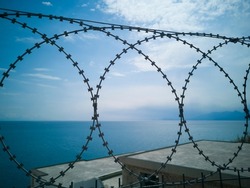 Fight for freedom symbol. Loops of spiked or razor wire curling around long stretches of barbed wire against a cloudy blue sky and blue sea, close up. Fight for freedom concept.