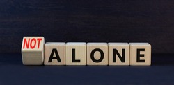 You are not alone symbol. Turned wooden cubes and changed concept words alone to not alone. Beautiful black table black background. Business, support and you are not alone concept. Copy space.
