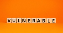 Vulnerable symbol. The word Vulnerable on wooden cubes. Beautiful orange table, orange background. Business and vulnerable concept. Copy space.