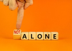 You are not alone symbol. Businessman turns wooden cubes and changes concept words alone to not alone. Beautiful orange background. Business, support and you are not alone concept. Copy space.