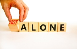 You are not alone symbol. Businessman turns wooden cubes and changes concept words alone to not alone. Beautiful white background. Business, support and you are not alone concept. Copy space.