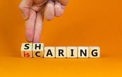 Sharing is caring symbol. Businessman turns wooden cubes with words 'sharing is caring'. Beautiful orange table, orange background. Business, sharing is caring concept. Copy space.