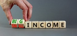 Big or small income symbol. Businessman turns wooden cubes and changes words Small income to Big income. Beautiful grey table grey background, copy space. Business big or small income concept.