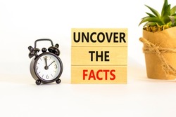 Uncover the facts symbol. Concept words Uncover the facts on wooden blocks on a beautiful white table white background. Black alarm clock. Business and uncover the facts concept. Copy space.