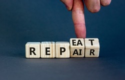 Repeat and repair symbol. Businessman turns wooden cubes and changes the word 'repeat' to 'repair'. Beautiful grey table, grey background, copy space. Business, repeat and repair concept.