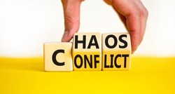 From conflict to chaos symbol. Concept words Conflict and Chaos on wooden cubes. Businessman hand. Beautiful yellow table white background. Business Conflict and Chaos concept. Copy space.