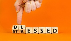 Blessed or stressed symbol. Businessman turns wooden cubes and changes the concept word Stressed to Blessed. Beautiful orange table orange background. Business blessed or stressed concept. Copy space.