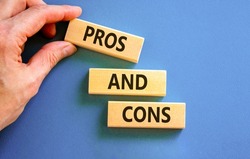 Pros and cons symbol. Wooden blocks with words 'Pros and cons'. Beautiful blue background, businessman hand. Business, pros and cons concept, copy space.