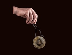 Hand holding bitcoin coin by strings. Manipulation in cryptocurrency exchanges, spoofing. Frauds with digital money. Controlling or artificially affecting price. High quality photo