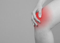 Banner with woman holding painful knee with red spot. Joint pain. Sprained, ruptured ligaments, meniscus tear, tendinitis, arthritis. Black and white. Copy space. High quality photo