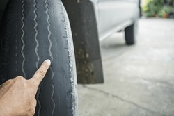 Close-up of man's hand pointing at old worn and bald tires from use. concept of tire wear and the dangers of using old tires.