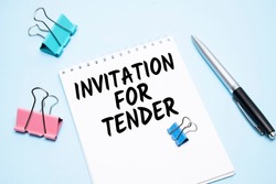 White notepad with text INVITATION FOR TENDER and office tools on the blue backgroundd
