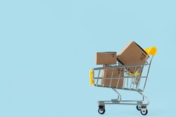 Toy shopping cart with boxes on blue background. Copy space for text or design. Sale, discount, shopping and delivery concept. Consumer society trend