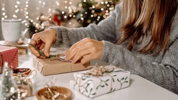 Woman s hands wrapping Christmas gift boxes, close up. Unprepared presents on white table with decor elements and items Christmas or New year DIY packing Concept.