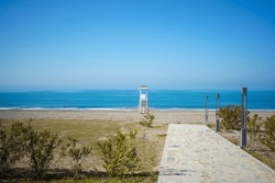 Scenic view of concrete pathway to the empty bay watch tower on a lonely seaside beach. Scenery landscape of a sea ocean shore with wooden abandoned lifeguard tower